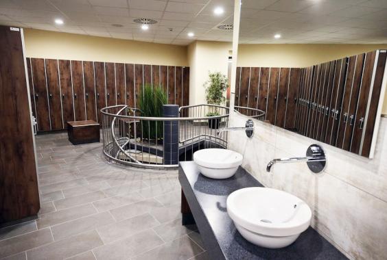 Moderne Umkleide mit Holzspinden, zwei weißen Waschbecken auf schwarzer Arbeitsplatte und Pflanzen in der Mitte