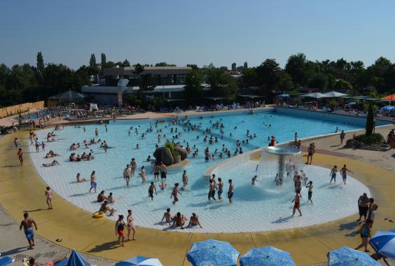 Belebtes Freibad mit vielen Menschen im Wasser und auf der Liegewiese an einem sonnigen Tag