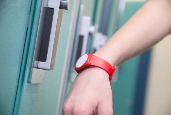 Hand mit rotem Armband hält vor einem elektronischen Türschloss an