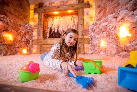 Mädchen spielt mit buntem Sandspielzeug in einem Raum mit Salzsteinwänden und warmem Licht