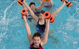 Mehrere Frauen im Schwimmbecken beim Aquagymnastik-Training mit orangen Wasserhanteln